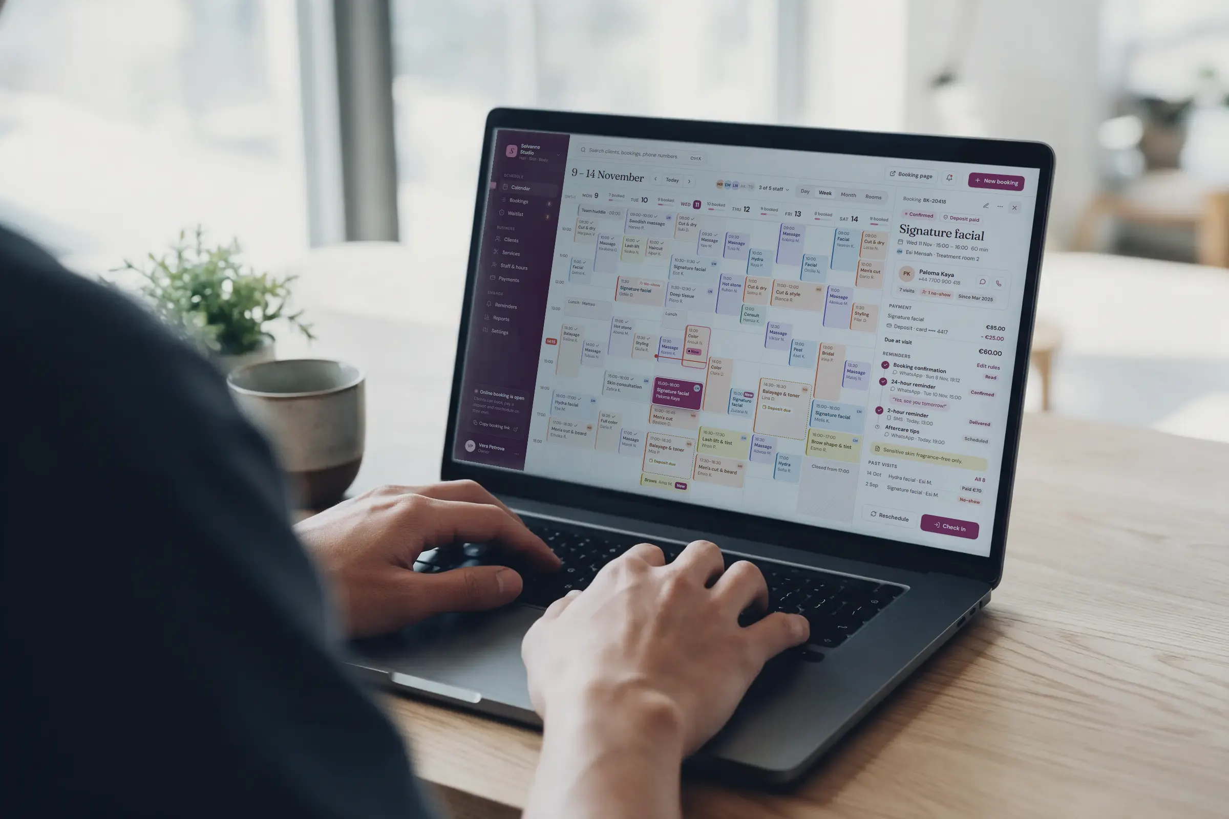 Hands typing on a laptop showing the booking system's staff calendar for the week