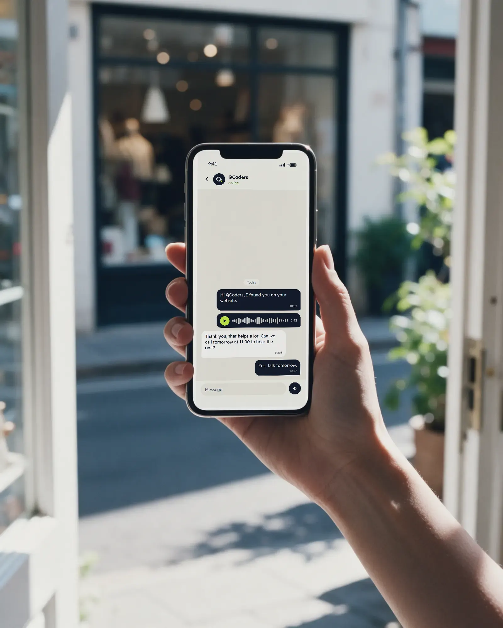 A hand holds up a phone in a bright shop doorway: a first message to Qcoders, a voice note, and the reply asking to call tomorrow at 11:00 to hear the rest